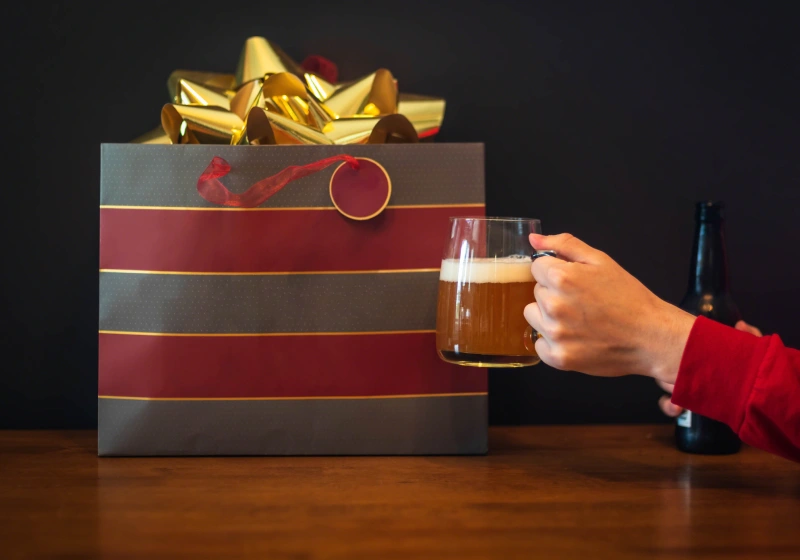mao segurando cerveja brindando com um pacote de presente